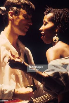 a man and woman standing next to each other with their hands on the guitar strings