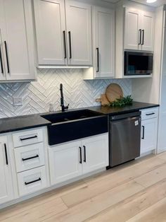 a kitchen with white cabinets, black counter tops and stainless steel dishwasher in the center