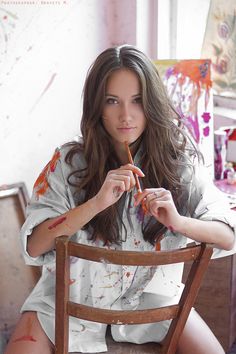 a woman sitting in a chair holding a piece of wood with paint all over her body