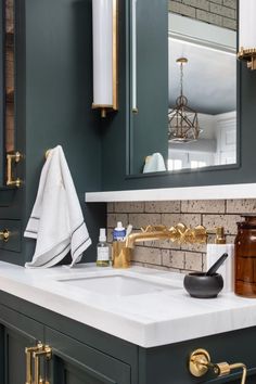 a bathroom with green cabinets and white counter tops, gold handles on the faucet