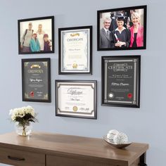 a table with flowers and pictures on the wall in front of it, along with other framed photos