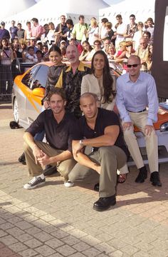 a group of people sitting on top of a car in front of a large crowd