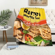 a blanket with noodles and vegetables on it in front of a white couch next to a potted plant