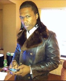 a man in a leather jacket is looking at his cell phone while wearing a fur collar