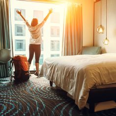 a woman standing in front of a window with her arms up and hands raised above the bed