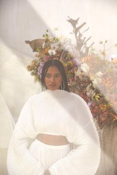 a woman standing in front of flowers with her hands on her hips