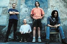 four men are sitting on benches in front of a graffiti - covered building with their arms crossed