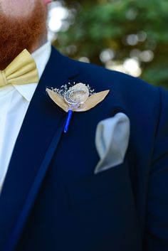 a man wearing a blue suit with a yellow bow tie and brooch on his lapel