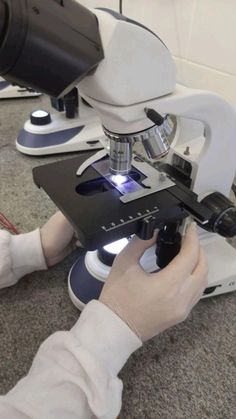 a person looking through a microscope at something in front of them with their hands on the table