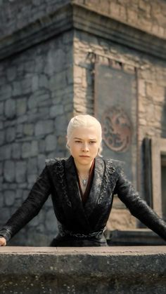 a woman with white hair sitting on top of a stone wall next to a building