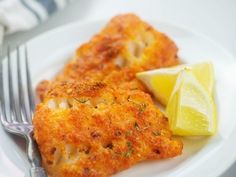 two pieces of fried fish on a plate with lemon wedges