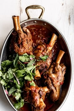 some meat and vegetables in a pan on a table with white wall behind the bowl