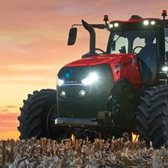 a red tractor with lights on driving through a corn field at sunset in the country