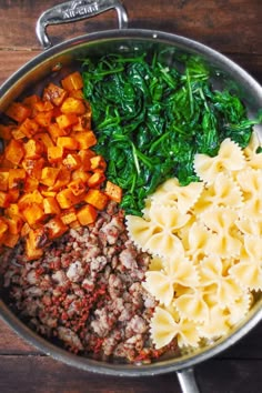 a pan filled with pasta, spinach and sweet potato wedges on top of a wooden table