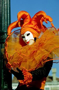 a person wearing a mask on top of a street pole with an orange dress and headdress