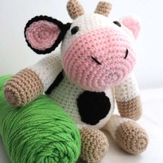 a crocheted cow sitting next to a green ball of yarn