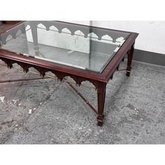 a glass top coffee table with metal legs and an intricately carved design on the bottom