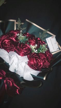 a bouquet of red roses and greenery sits on a black cloth with gold trim