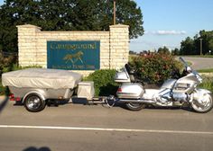 a motorcycle with a trailer attached to it parked in front of a sign that says the equestrian club