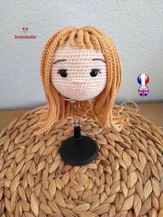 a knitted doll sitting on top of a woven table cloth with a black base