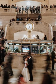 a bride and groom standing in front of a clock at the grand central train station