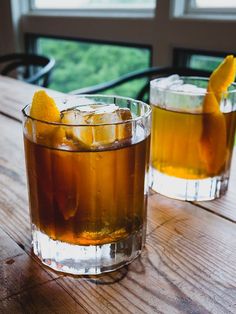 two glasses filled with drinks sitting on top of a wooden table