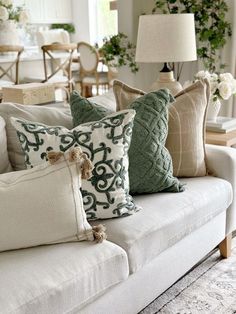 a white couch with pillows on top of it in front of a table and chairs