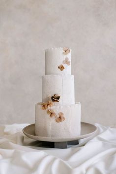 a three tiered white cake with flowers on it sitting on a gray platter