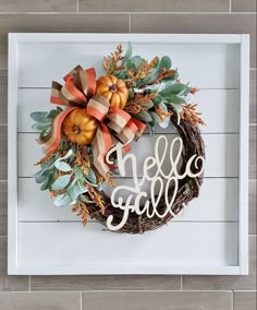 a wreath with the word hello fall is hanging on a white frame against a wood wall