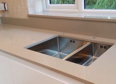 two stainless steel sinks in a white countertop next to a window with plants outside