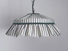 a white and gray striped lamp hanging from a metal hook with green trim on it