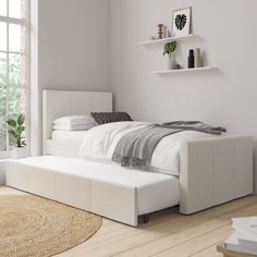 a white bed sitting on top of a wooden floor next to a wall mounted shelf