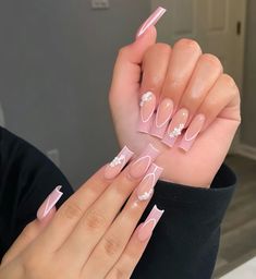 a woman holding up her nails with pink and white designs on the tip of it