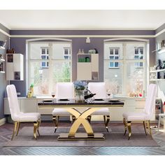 a dining room table with white chairs and a gold x on the top, in front of two windows