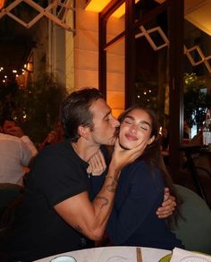 a man and woman sitting at a table kissing