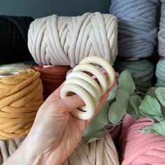 a hand is holding several different colored yarns in front of some green and white plants