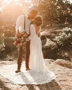 a bride and groom standing on top of a rock with the sun shining through them