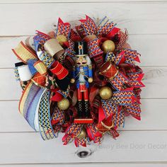 a christmas wreath with a nutcracker figure on the front and red, blue, gold and white ribbons