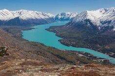 the view from top of a mountain looking down at a lake and snow covered mountains