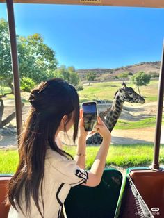 a woman taking a photo of a giraffe in an enclosure with her cell phone