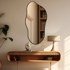 a mirror on the wall next to a table with a lamp and bookcase behind it