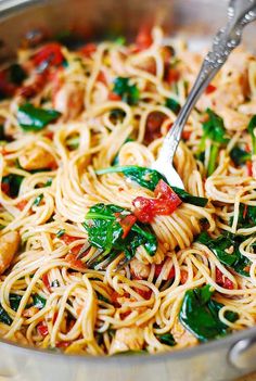 a pan full of pasta with spinach and tomato sauce being stirred by a fork