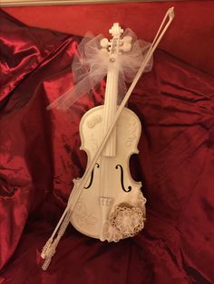 a white violin with a veil on it's head sitting on a red cloth