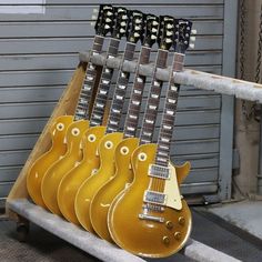 five guitars are lined up on a rack in front of a garage door and one is yellow