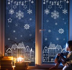 a child sitting on a window sill looking out at snowflakes