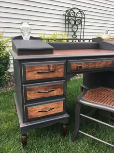 an old desk is painted black and brown with wood trimming on the top, along with a wicker chair