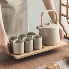 a person holding a tray with cups and a tea pot on it, next to some cookies