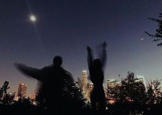 two people standing in front of a city skyline at night with their arms raised up