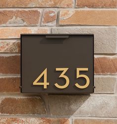 a black and gold mailbox mounted to a brick wall with the number 435 on it