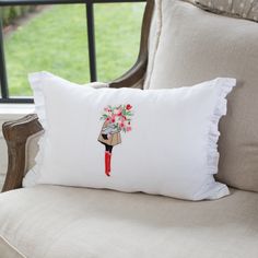 a white pillow sitting on top of a chair next to a window with flowers in it